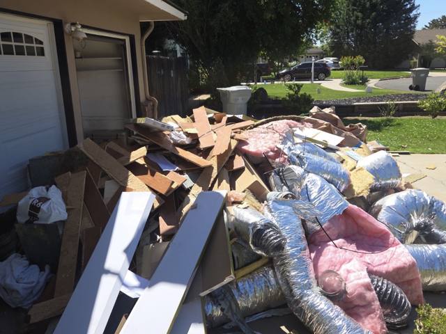 Driveway of a customer's home covered in remodel debris including cut flooring, drywall, fiberglass insulation and flexible ductwork before removal
