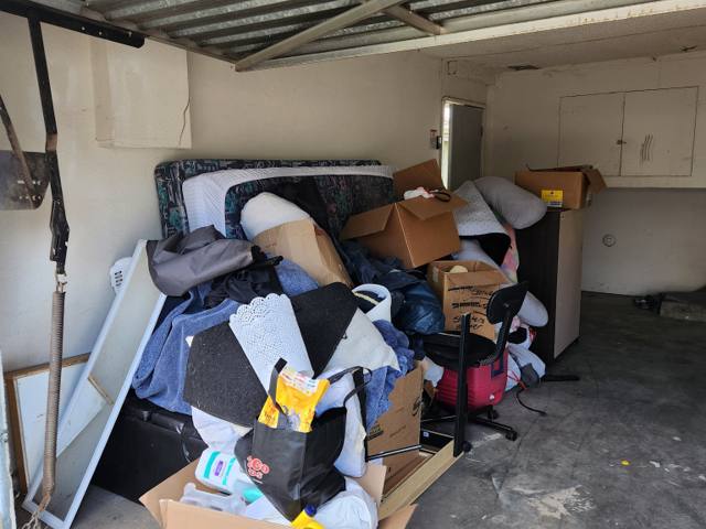 Single-car garage packed to the ceiling with mattresses, box springs, cardboard boxes, bedding and an office chair before a Rapid Haul cleanout